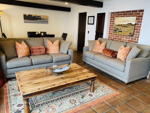 Cozy living room with two gray sofas, orange pillows, a wooden coffee table, and a patterned rug.