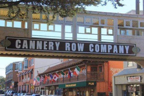 Sign for Cannery Row Company with flags from various countries and buildings in the background.