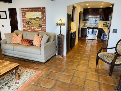 Cozy living area with a sofa, decorative pillows, wooden coffee table, and a view of a kitchen with dark cabinets.