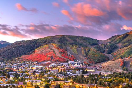 A scenic view of a mountain town with vibrant autumn foliage and colorful clouds at sunset.