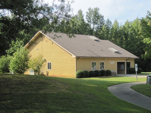 A yellow building surrounded by trees and grass, with a pathway leading to the entrance.