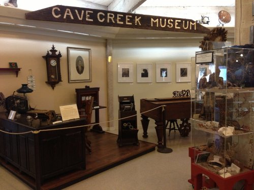 Interior of Cave Creek Museum featuring historical artifacts, a wooden sign, and a display case with various items.