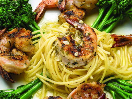 A plate of pasta topped with grilled shrimp and garnished with broccolini.