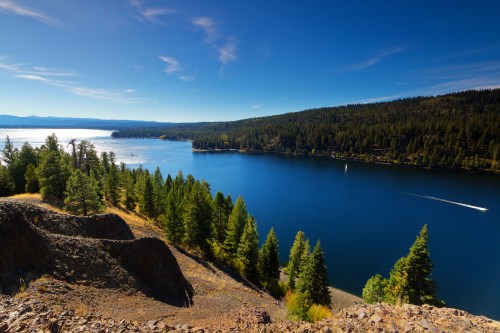 A serene lake surrounded by lush green trees and mountains under a clear blue sky.