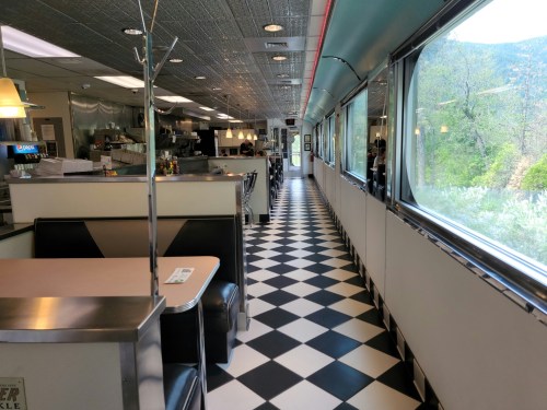 A diner interior with black and white checkered floor, booths, and large windows showing a scenic view outside.