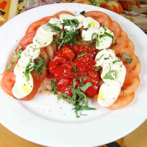 A plate of sliced tomatoes topped with mozzarella, basil, and a drizzle of sauce, garnished with herbs and spices.