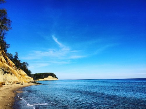 A serene beach scene with sandy shores, cliffs, and a clear blue sky over calm waters.
