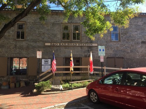 Exterior of the B&O Railroad Station, featuring stone walls, flags, and a red car parked nearby.