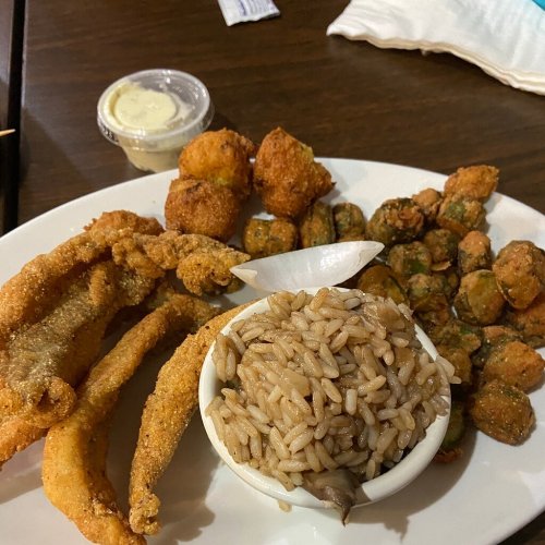 A plate of fried fish, rice, fried okra, and hushpuppies, served with a small cup of dipping sauce.