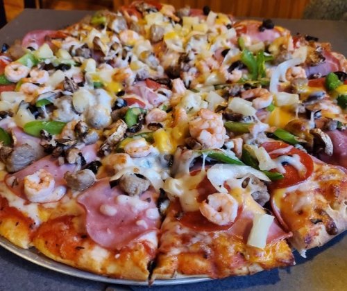 A large pizza topped with shrimp, mushrooms, green peppers, onions, and various meats, sliced into wedges.