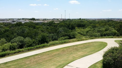 A winding pathway leads through lush greenery, with a distant view of buildings and a clear blue sky.