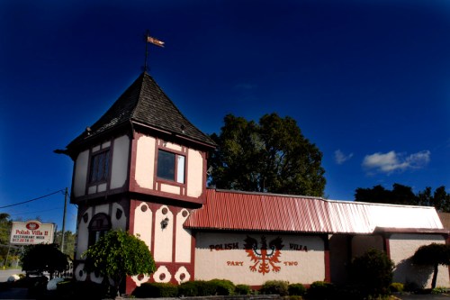 A charming building with a tower, featuring red and white accents, labeled "Polish Villa II" against a blue sky.