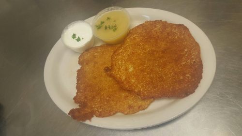 Two golden-brown fried patties on a plate, served with a side of sour cream and applesauce.