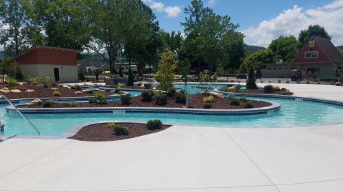 A winding pool surrounded by landscaped gardens and trees under a clear blue sky.