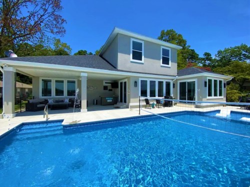 Modern house with a pool, surrounded by trees and outdoor seating, under a clear blue sky.