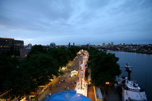 A scenic view of a riverside promenade at dusk, with trees, lights, and people enjoying the area.