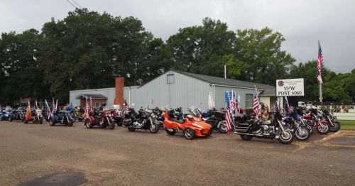A line of motorcycles parked outside a building, with flags displayed, on a cloudy day.