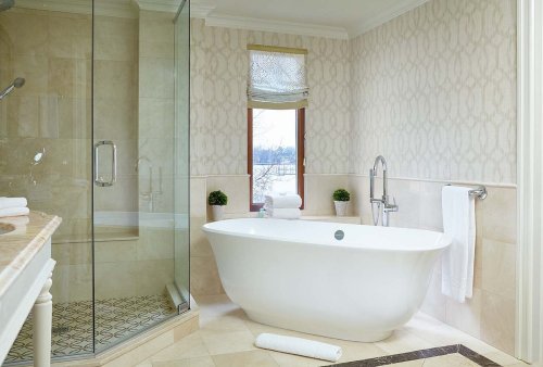 A modern bathroom featuring a freestanding tub, glass shower, and elegant wallpaper with decorative plants.