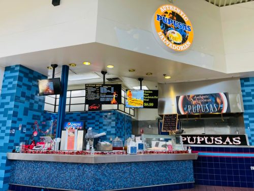 A colorful food stall featuring a sign for "Authentic Pupusas" with a menu and various food items displayed.