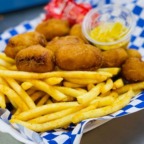 A basket of golden fries with several fried snacks and a small cup of dipping sauce on the side.