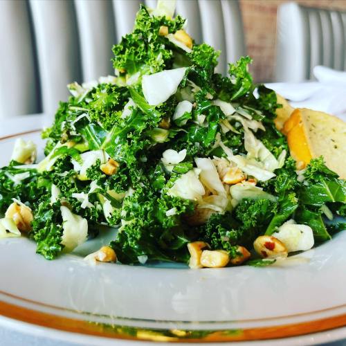 A vibrant salad with kale, cabbage, and chopped nuts, garnished with a lemon wedge on a decorative plate.