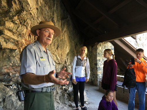 A park ranger speaks to a small group of visitors inside a stone structure, with a mix of engaged expressions.