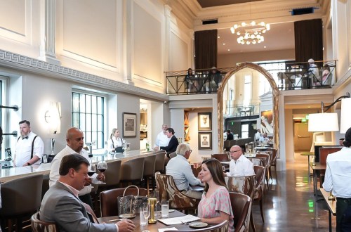 A stylish restaurant interior with diners at tables, servers attending, and a spacious, elegant atmosphere.