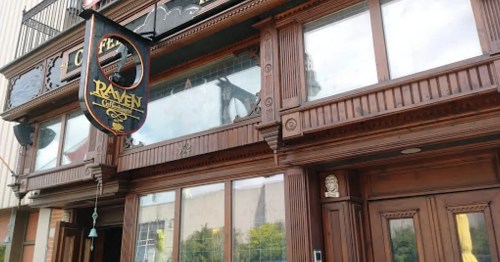 Exterior of a wooden pub with a sign reading "Raven" and large windows, showcasing a classic architectural style.