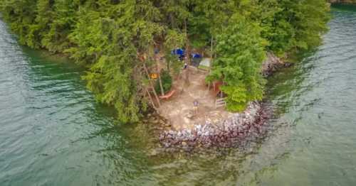 Aerial view of a small island surrounded by water, featuring trees, tents, and a rocky shoreline.