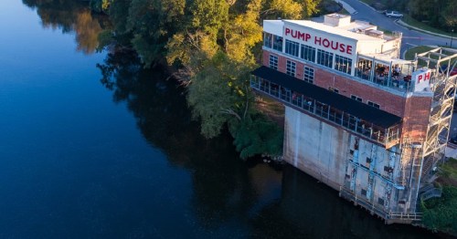 Aerial view of the Pump House building by a river, surrounded by trees and reflecting water.