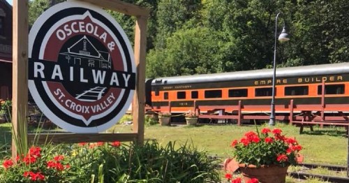 Sign for Osceola & St. Croix Valley Railway with a vintage train and flowers in the foreground.