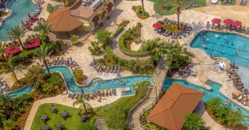 Aerial view of a resort pool area with winding water features, lounge chairs, and palm trees.