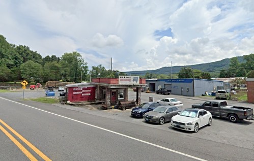 A roadside view of a small business with parked cars and mountains in the background under a cloudy sky.