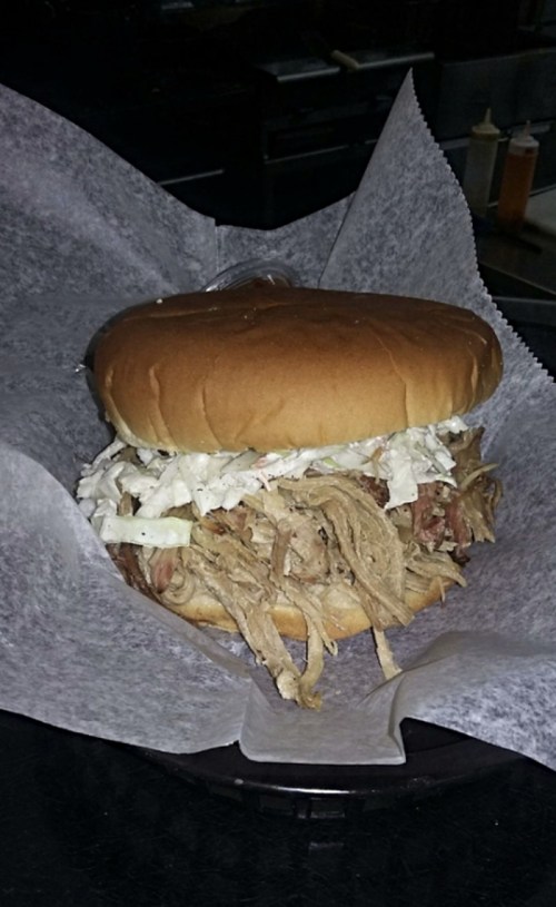 A pulled pork sandwich topped with coleslaw, served in a basket lined with parchment paper.