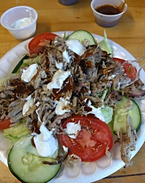 A plate of salad topped with shredded meat, tomatoes, cucumbers, and drizzled with sauces.