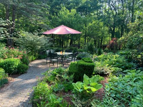A serene garden with a stone path, lush greenery, and a table under a pink umbrella surrounded by vibrant plants.
