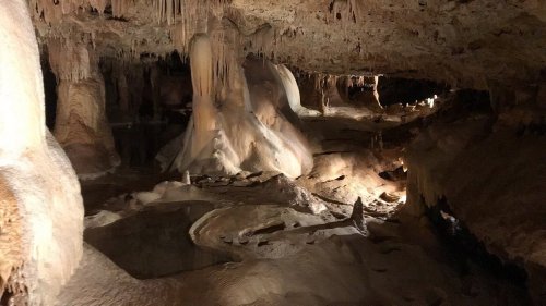 A dimly lit cave interior featuring stalactites, stalagmites, and reflective water surfaces.