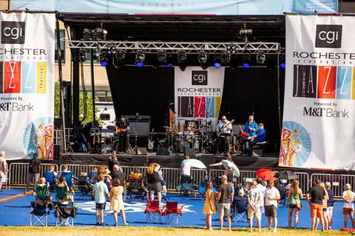 A lively outdoor jazz concert with a band on stage and an audience seated on the grass, enjoying the performance.