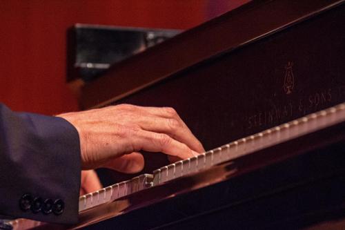A close-up of a hand playing the keys of a Steinway piano, with a blurred background.