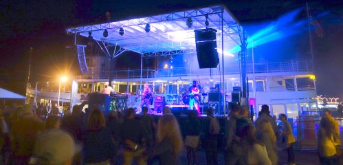 A lively outdoor concert at night with a band performing on stage and an audience enjoying the music.
