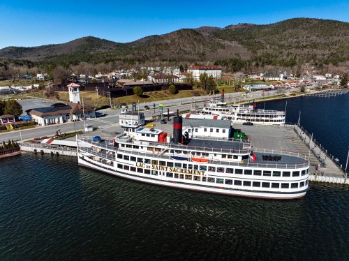 A large white steamboat docked at a pier with mountains in the background and a clear blue sky.