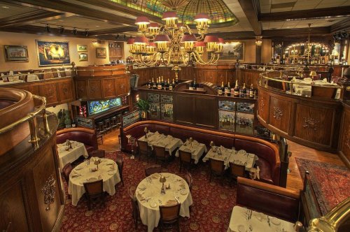 Elegant restaurant interior with chandeliers, wooden decor, and tables set for dining in a cozy atmosphere.