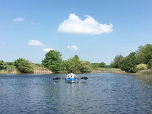 A person kayaking on a calm waterway surrounded by lush greenery and blue skies with fluffy clouds.