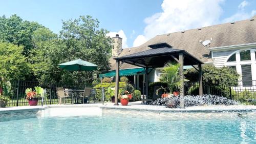 A serene backyard pool area with a gazebo, lush greenery, and patio furniture under a clear blue sky.