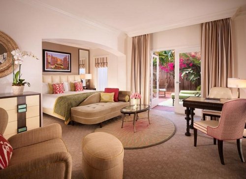 A stylish hotel room featuring a bed, seating area, and patio access, adorned with colorful decor and natural light.