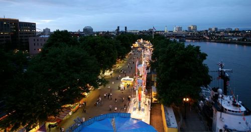 A scenic view of a riverside promenade at dusk, lined with trees and illuminated attractions.