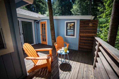 A cozy outdoor deck with two orange chairs, a small blue table, and surrounded by trees.