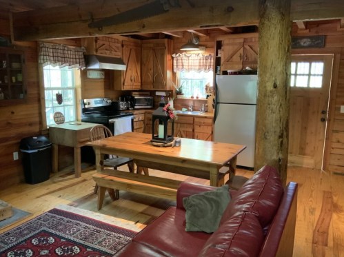 Cozy wooden cabin interior featuring a kitchen, dining table, and living area with a red sofa and rustic decor.