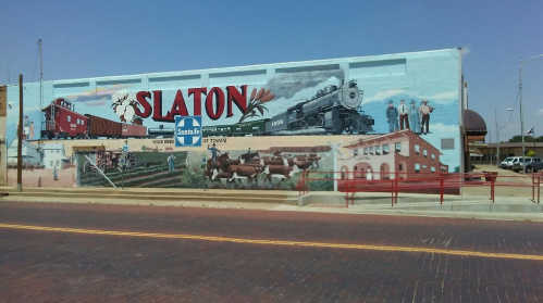 Mural depicting Slaton's history, featuring a train, farming scenes, and local landmarks on a blue wall.