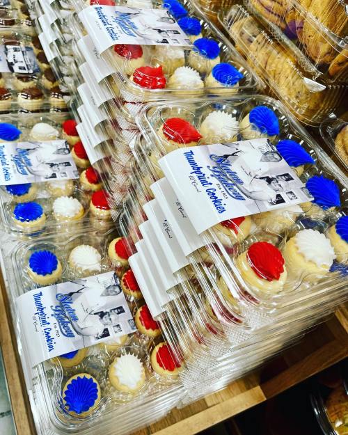 A display of colorful cookies in clear containers, featuring red, white, and blue frosting, stacked on a wooden shelf.